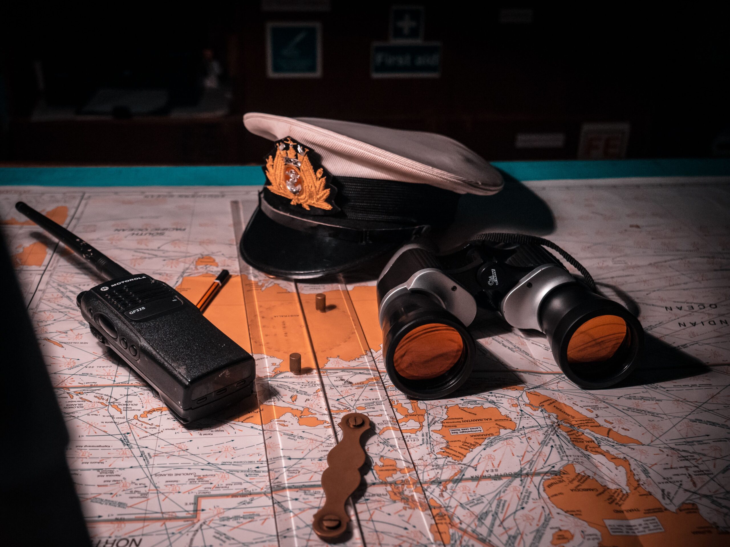 Close-up of ship captain's tools on a map, including hat, binoculars, and radio.